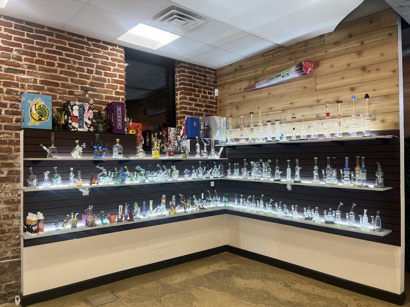 A corner wall of shelves holding dozens of hand-blown glass water pipes and rigs, each shelf lit from beneath.