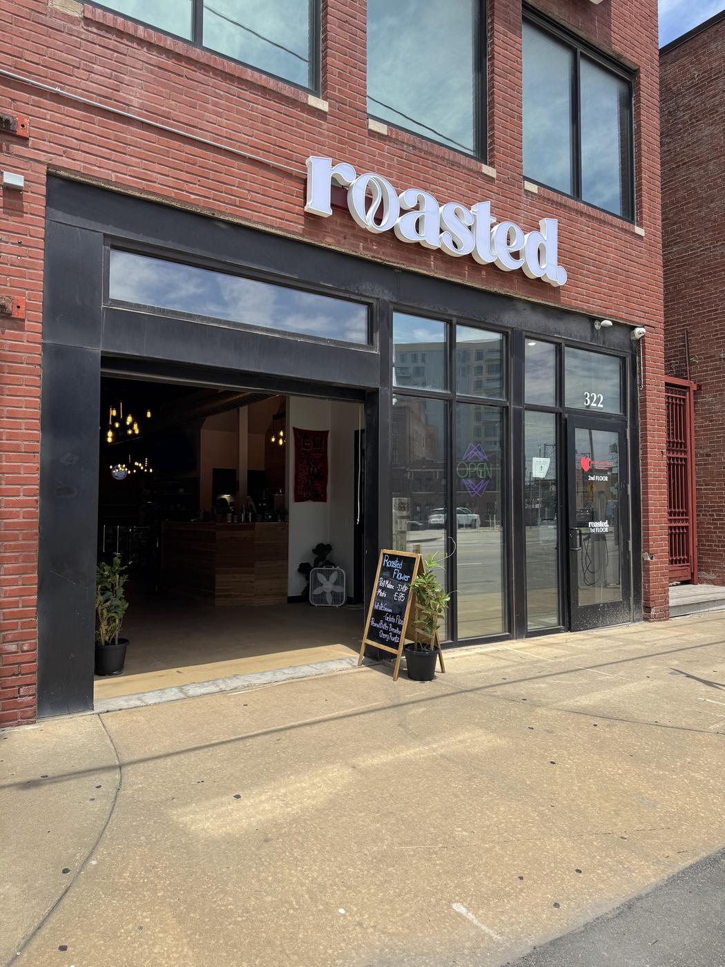 The roasted. storefront on Southwest Boulevard: white lettering on red brick above a roll-up garage door standing open, with a chalkboard on the sidewalk.